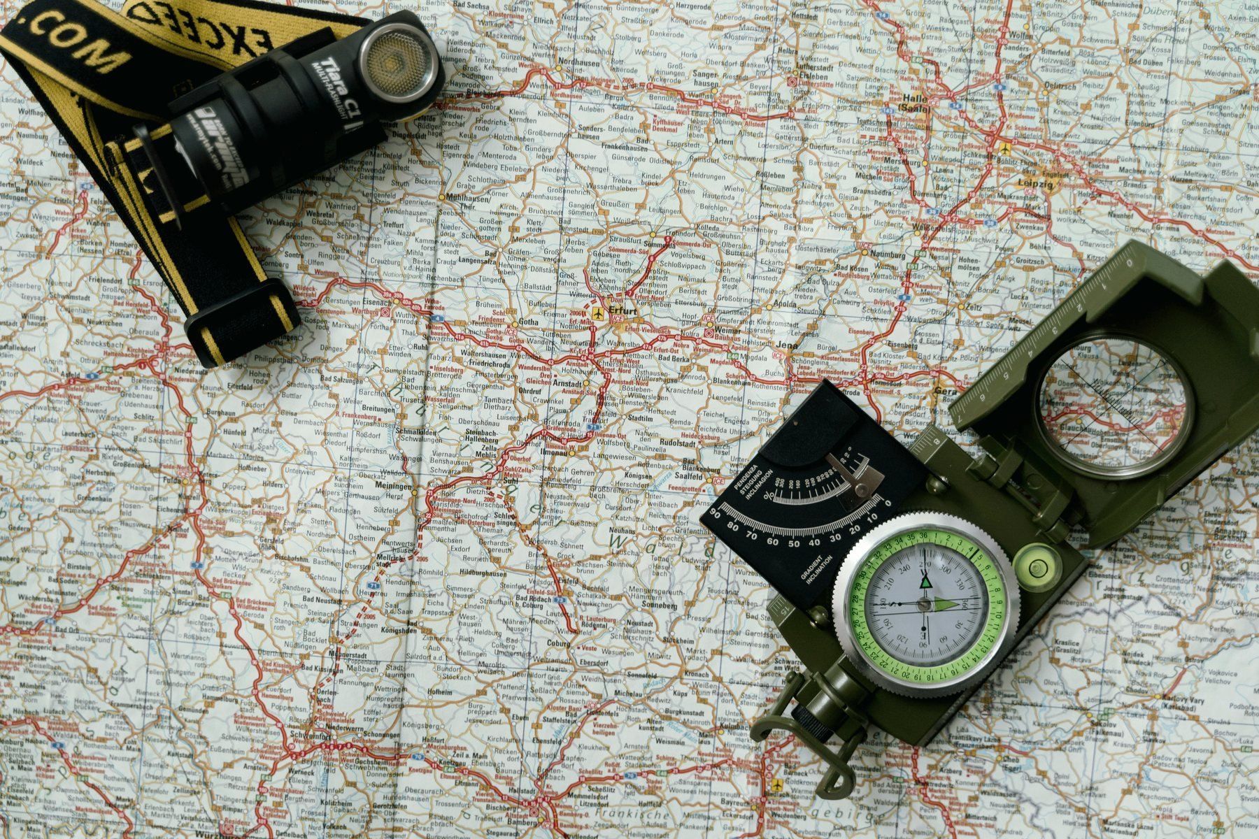 A road map with a compass and a flashlight laid on top.