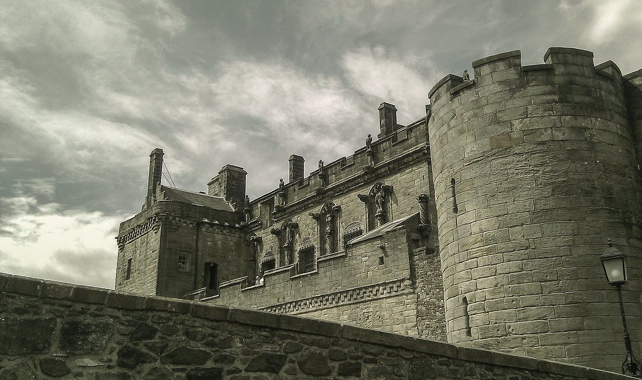 The stone walls and round tower of Stirling Castle against a cloudy sky.