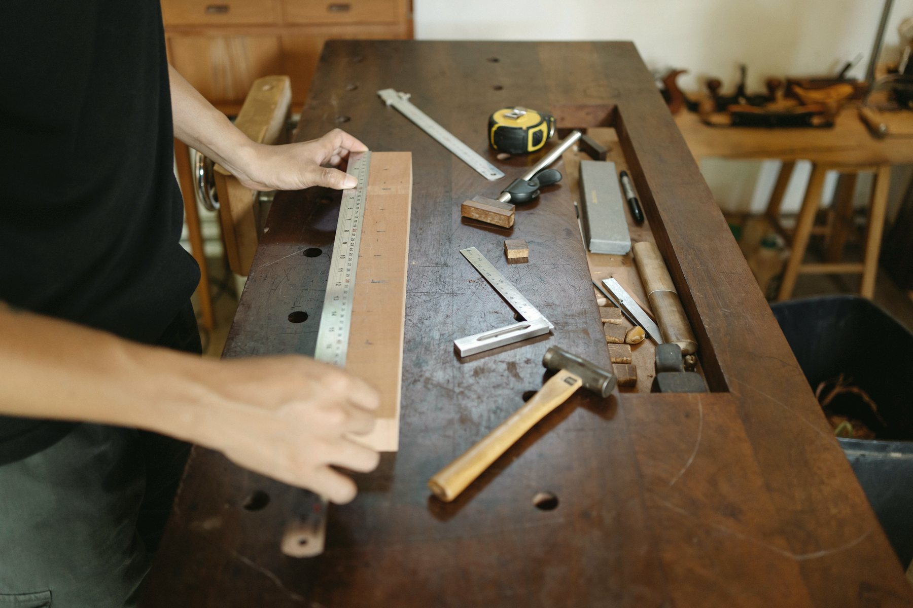 Hands measuring a piece of timber with a ruler on a workbench.