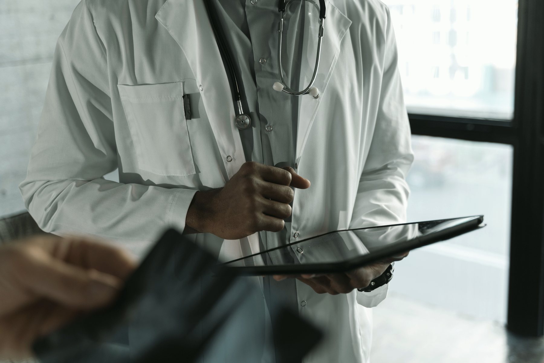 A clinician in a white coat reviewing notes on a tablet.
