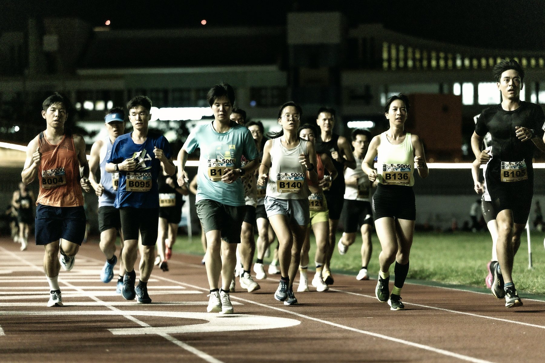 A field of runners mid-race on a floodlit track.