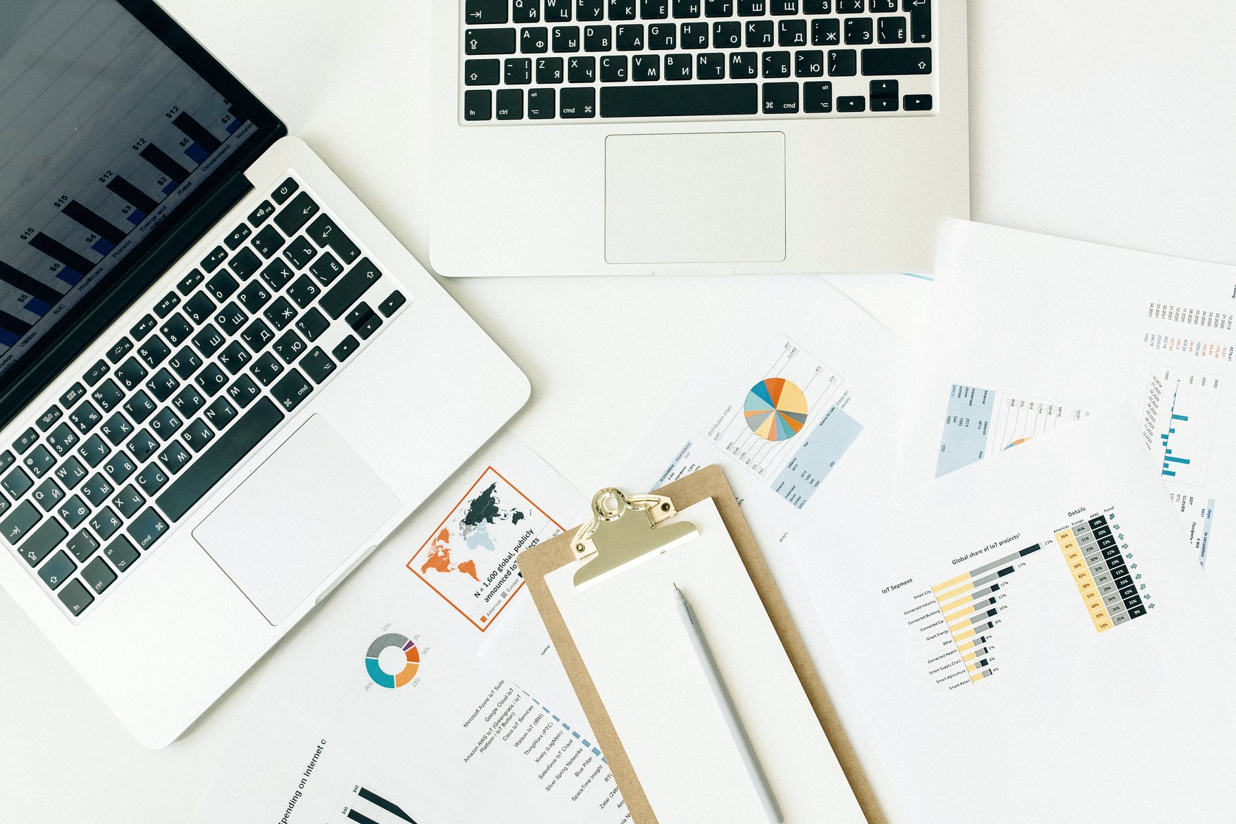 Overhead view of laptops, charts and printed reports on a white desk.