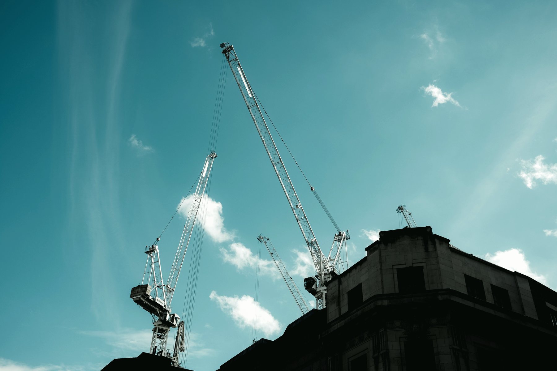 Construction cranes rising against a clear blue sky.