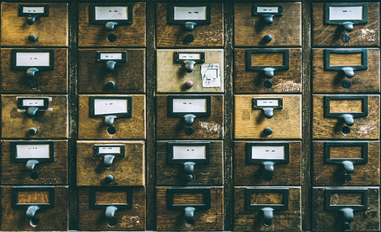 Rows of wooden card-catalogue drawers, each with a metal handle and a small label, some labels filled in and some blank.