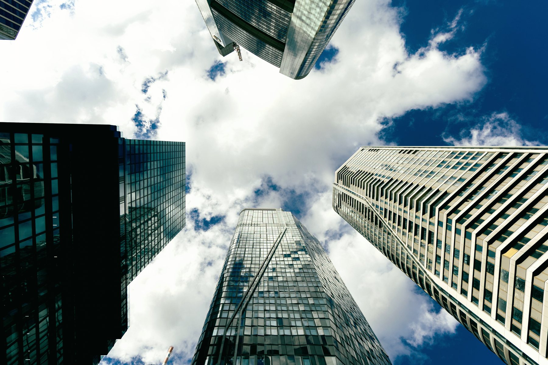 Glass office towers seen from the street, looking up into a cloudy sky.