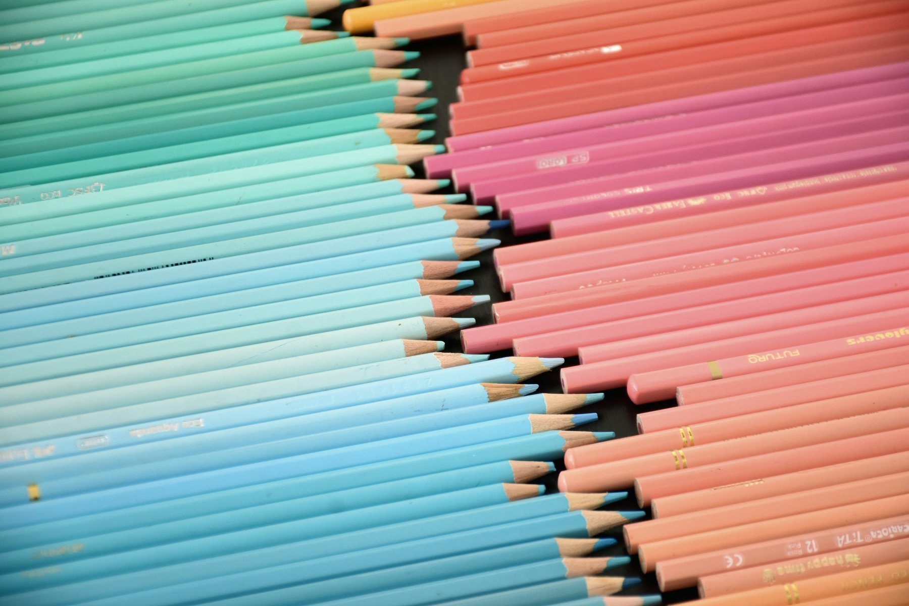 Coloured pencils laid out in a graded arrangement from blue to pink.